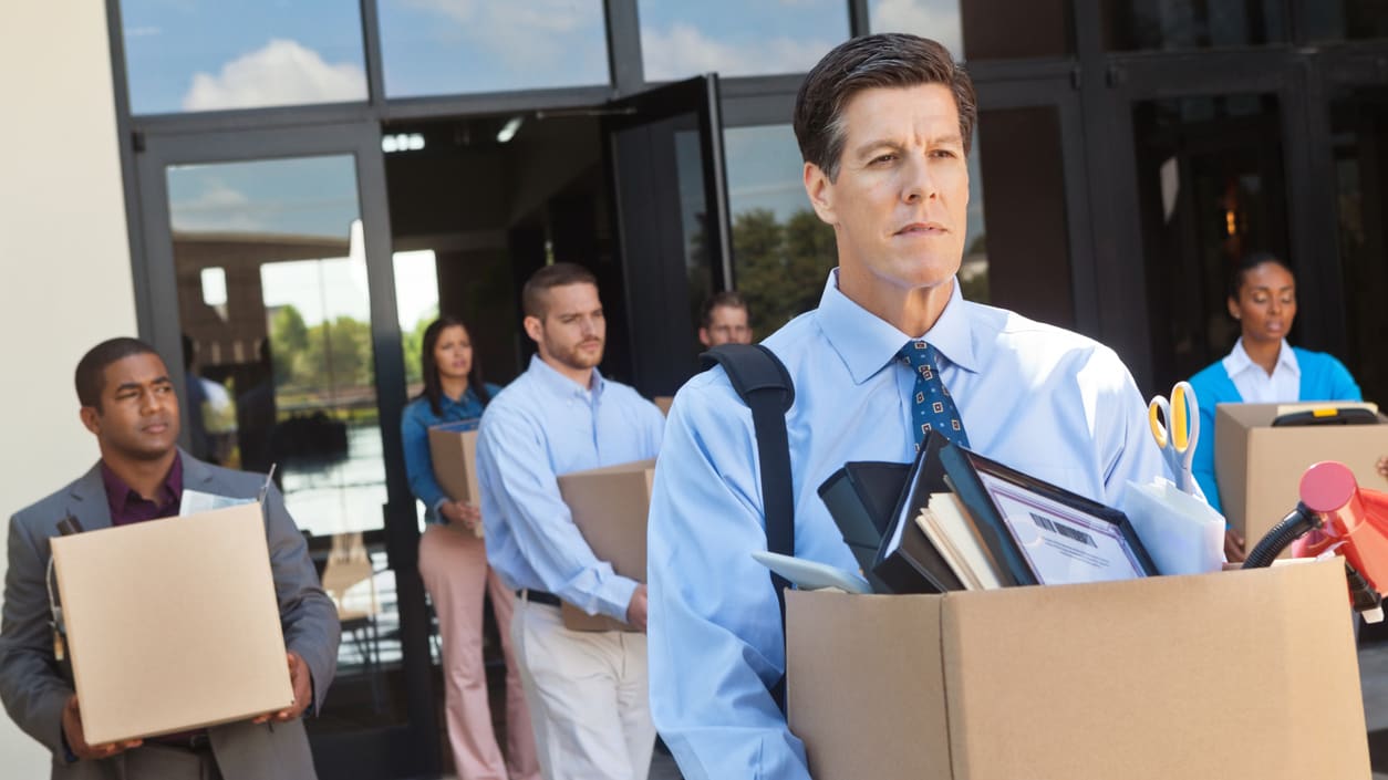 A group of business people carrying boxes out of a building.
