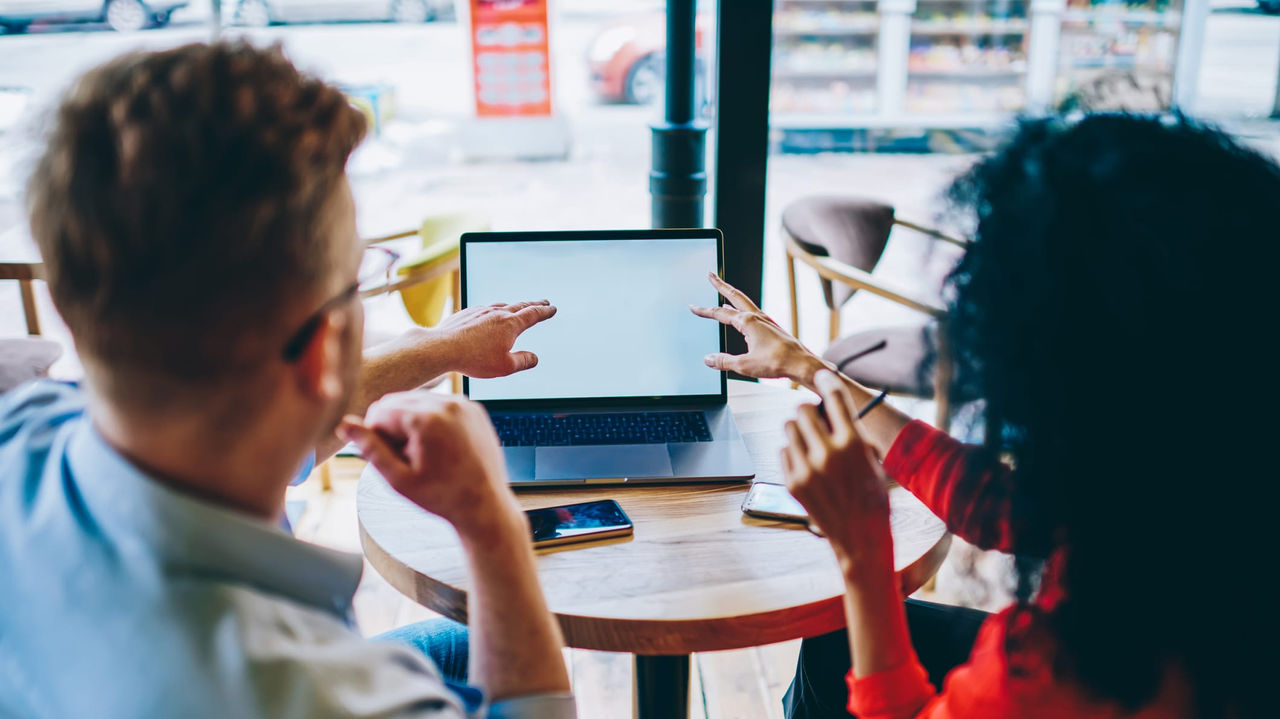 Two people sitting at a table looking at a laptop.