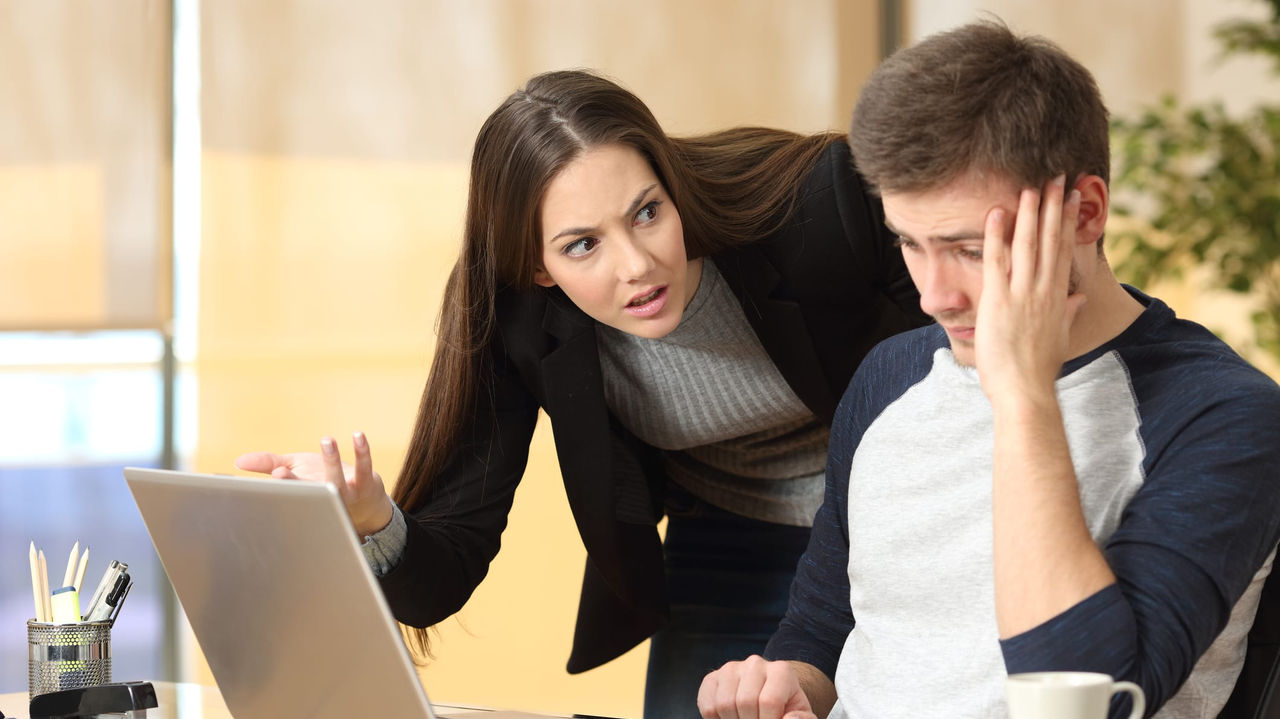 A man and woman are looking at a laptop in an office.