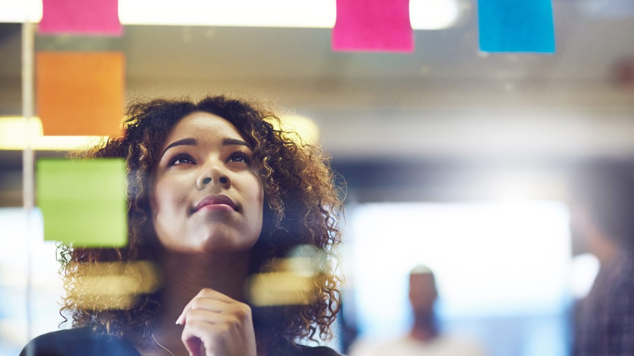 A woman looking at sticky notes on a glass wall.