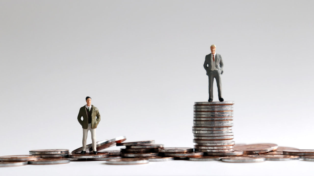 Two business men standing on top of a stack of coins.