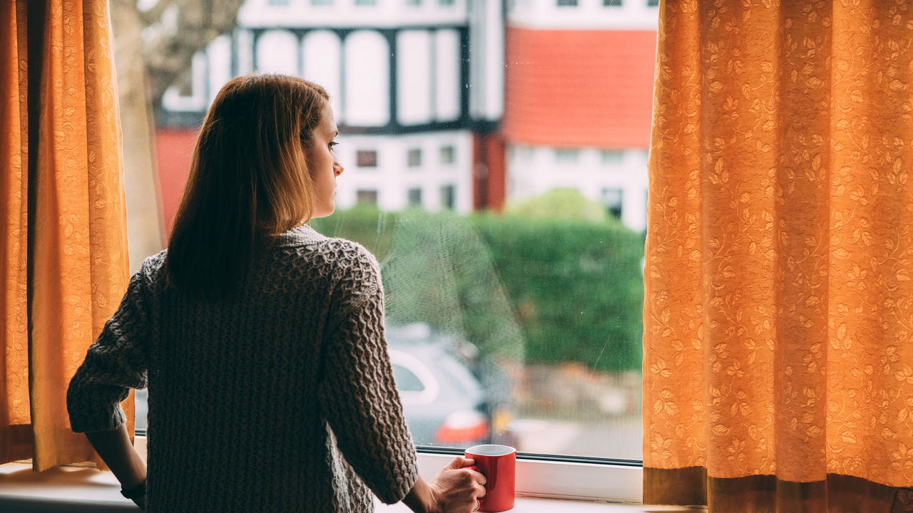 A woman looking out of a window with a cup of coffee.