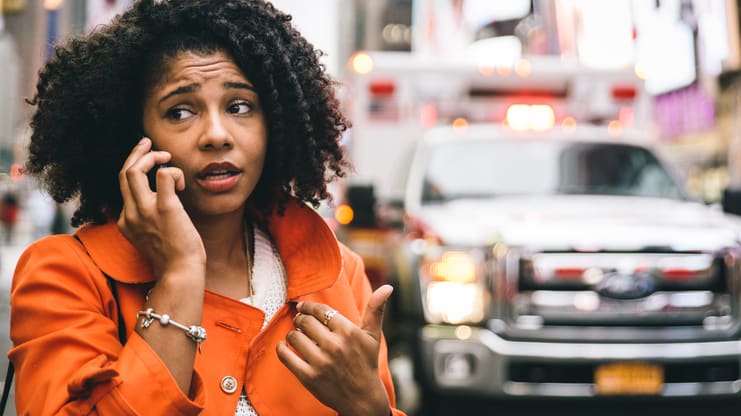 A woman talking on a cell phone in front of an ambulance.