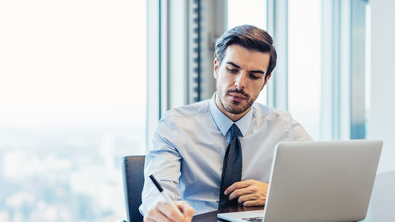 A businessman sitting at a desk with a laptop and a pen.