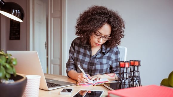 A woman sitting at a desk with a laptop and a notebook.