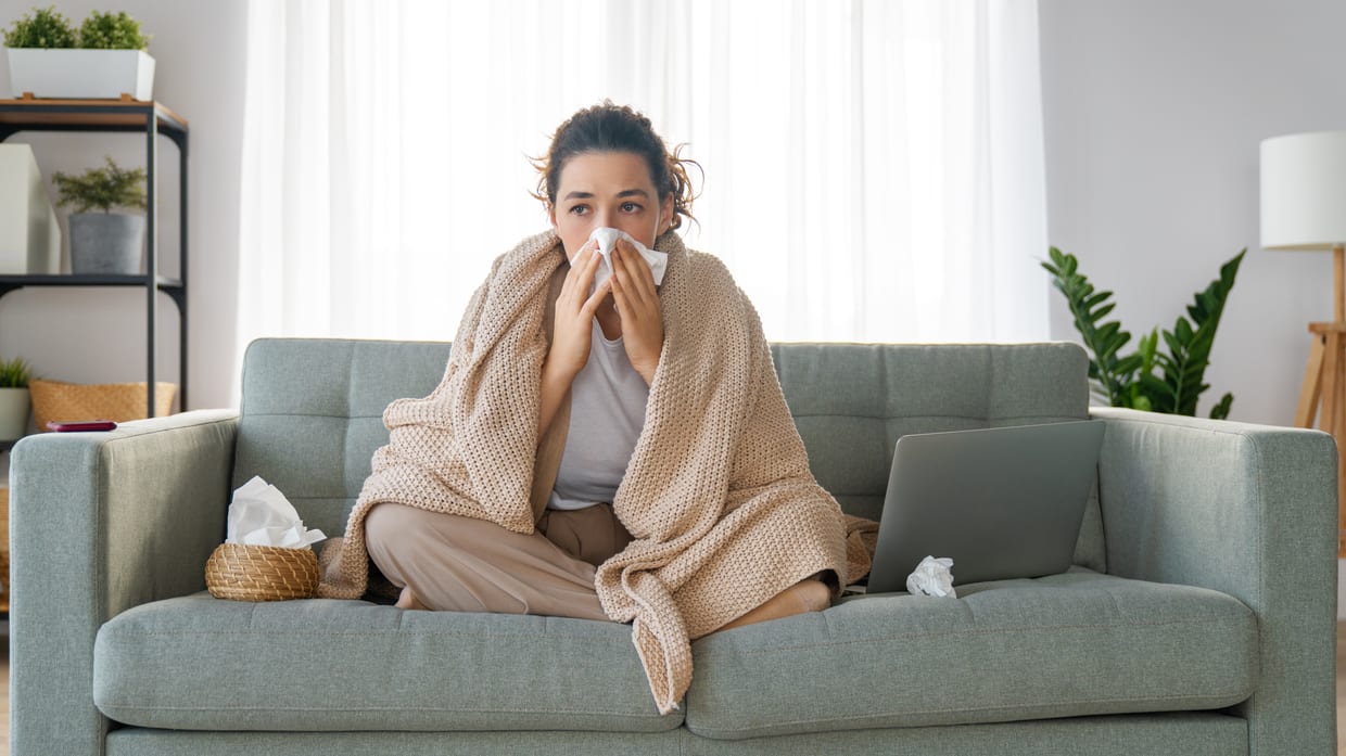 A woman sitting on a couch with a blanket covering her nose.