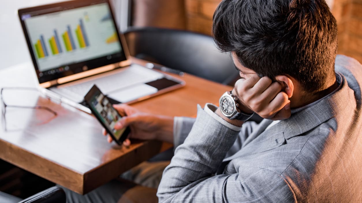 A businessman sitting at a table with a laptop and cell phone.