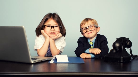 Two children in glasses sitting at a desk with a laptop.