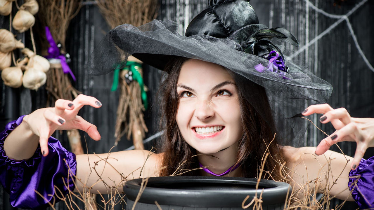 A woman in a witch hat is holding a pot of witches brew.