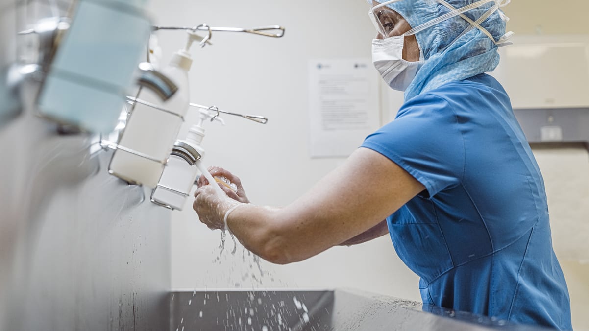 A woman in scrubs washing her hands in a bathroom.