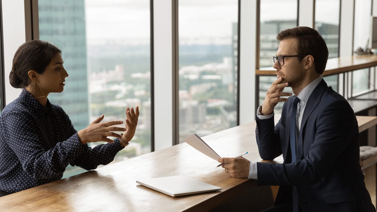 A man and woman talking at a desk in an office.