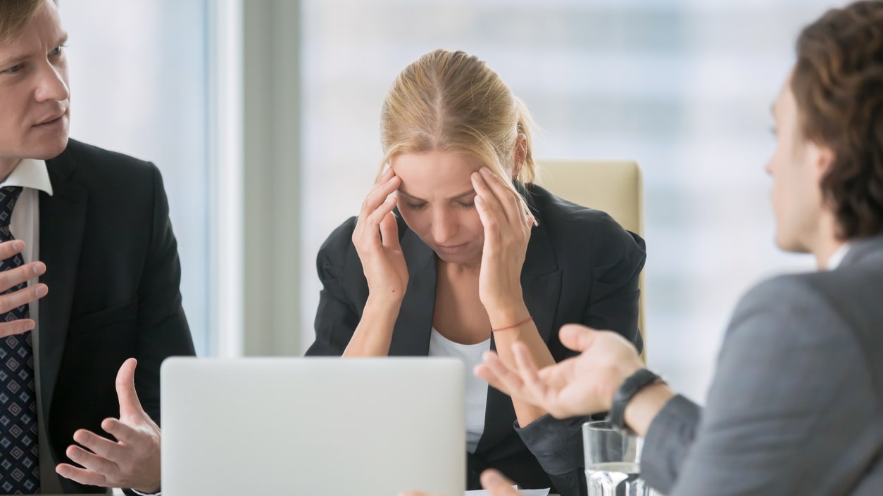 A group of business people sitting at a table with their heads in their hands.