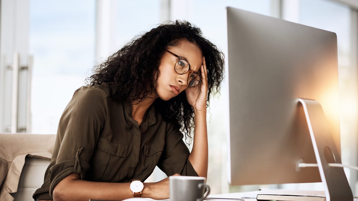 A woman is sitting in front of a computer with her hand on her head.