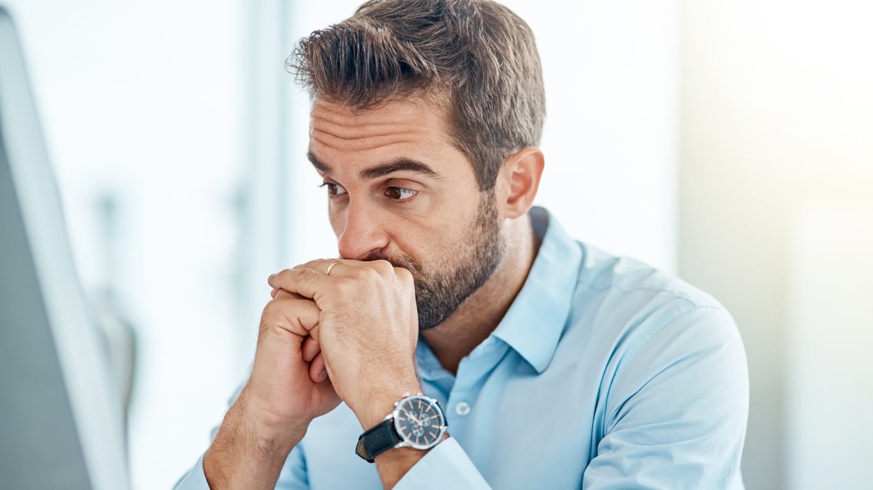 A man sitting in front of a computer with his hand on his chin.