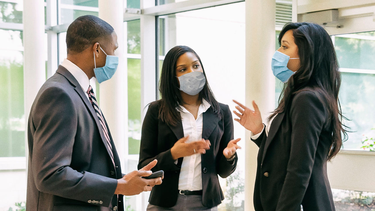 Three business people wearing face masks talking to each other.
