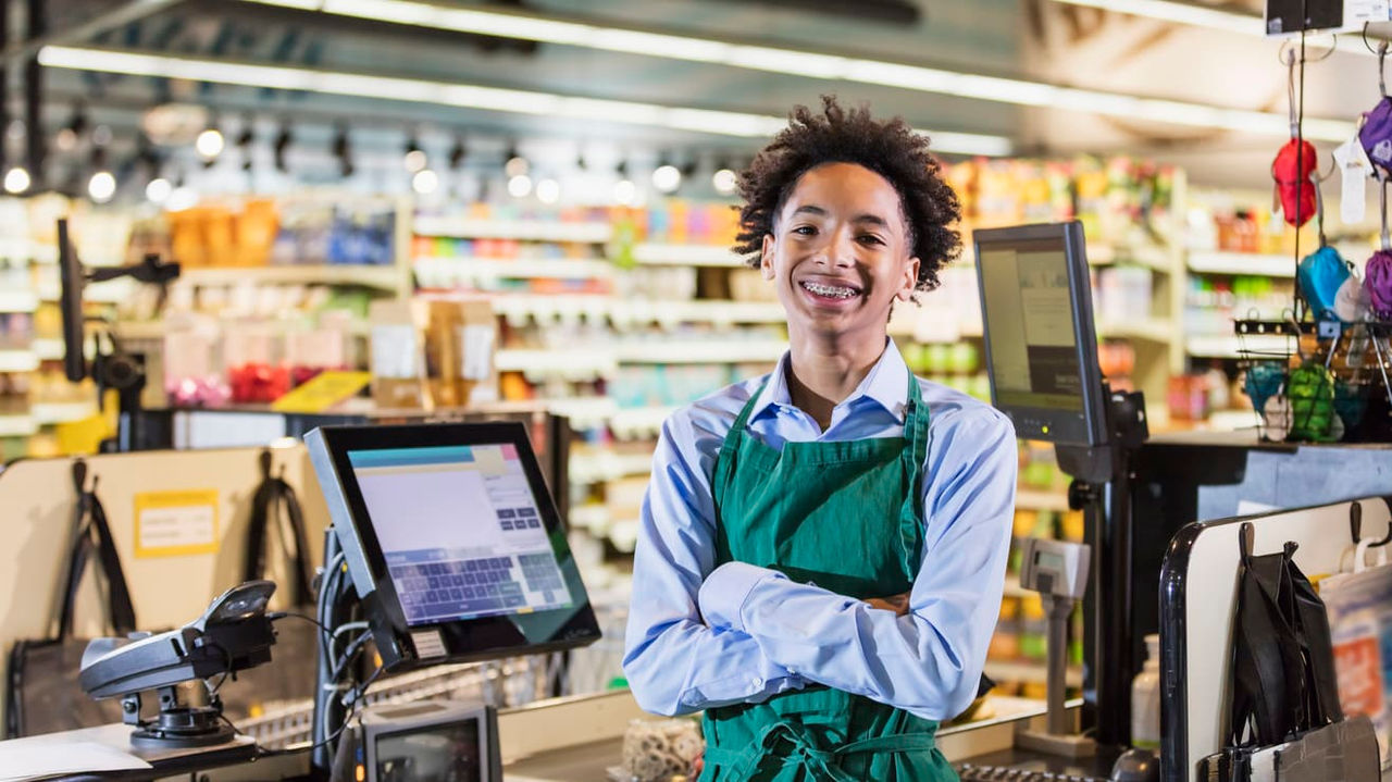 A young woman in a green apron standing in a grocery store.