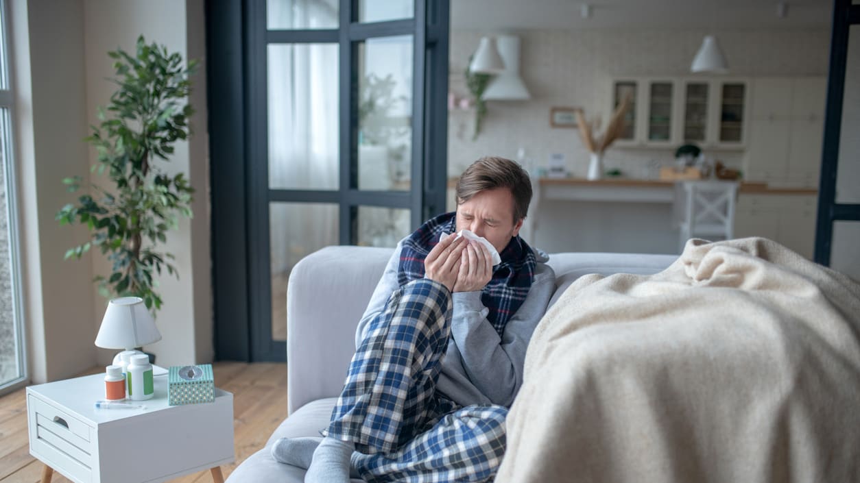 A man sitting on a couch blowing his nose.