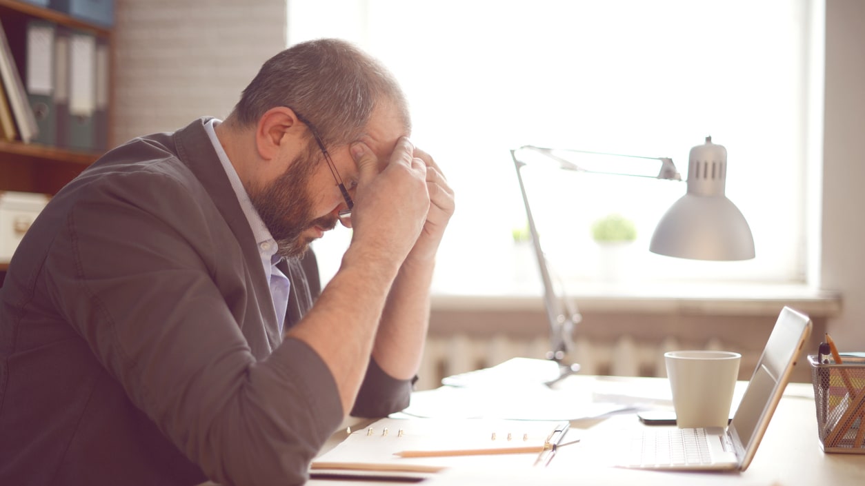 A man is sitting at his desk with his head in his hands.