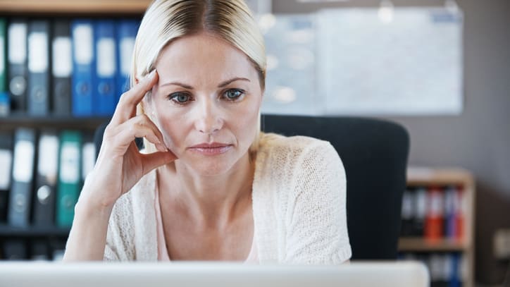 A woman sitting in front of a laptop with her hand on her head.