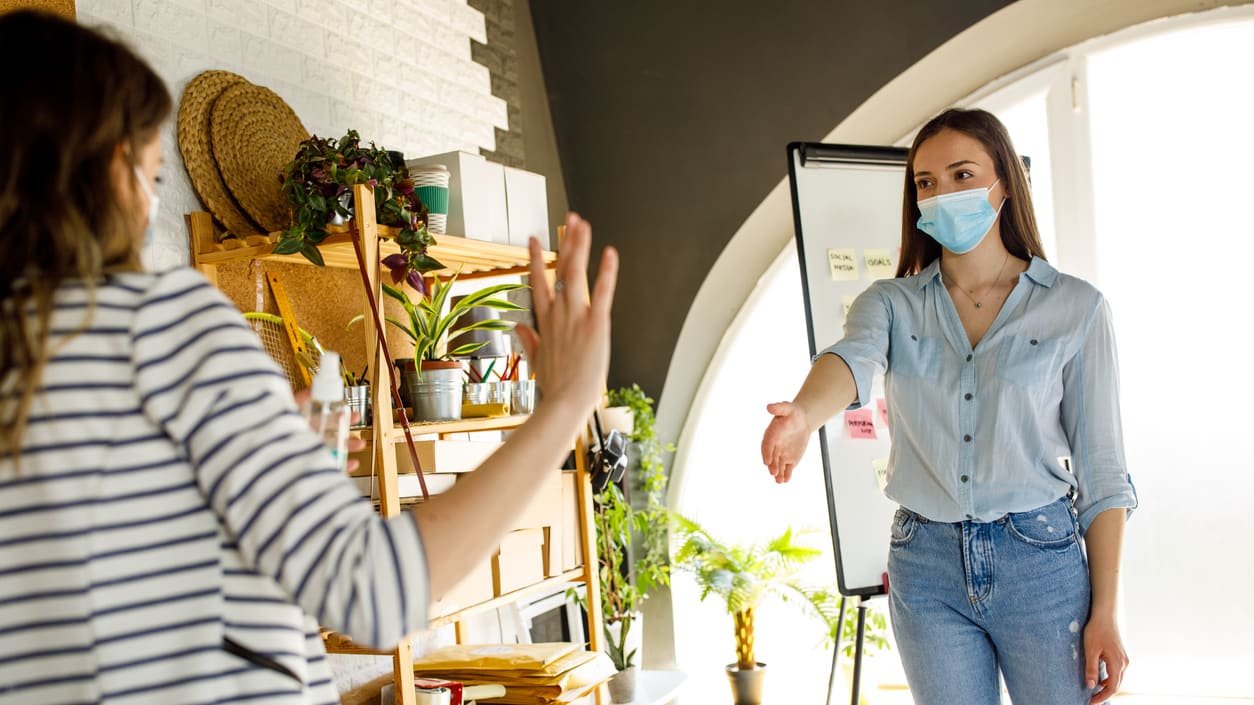 A woman wearing a face mask is talking to another woman in an office.