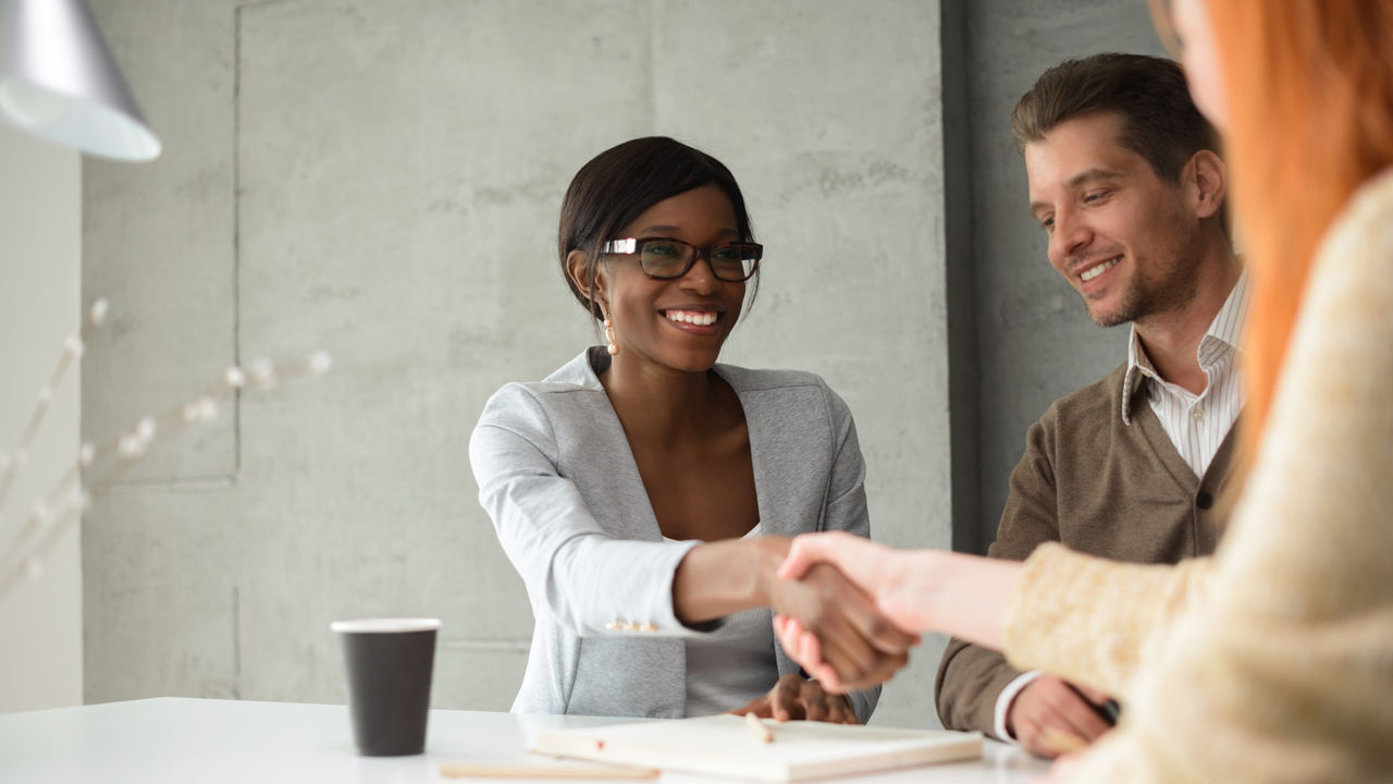 Two people shaking hands at a table in an office.