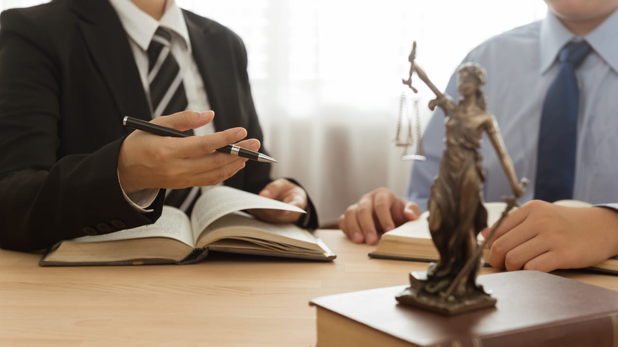 A man and woman sitting at a table with a statue of a judge.