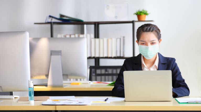 A woman wearing a face mask at her desk.