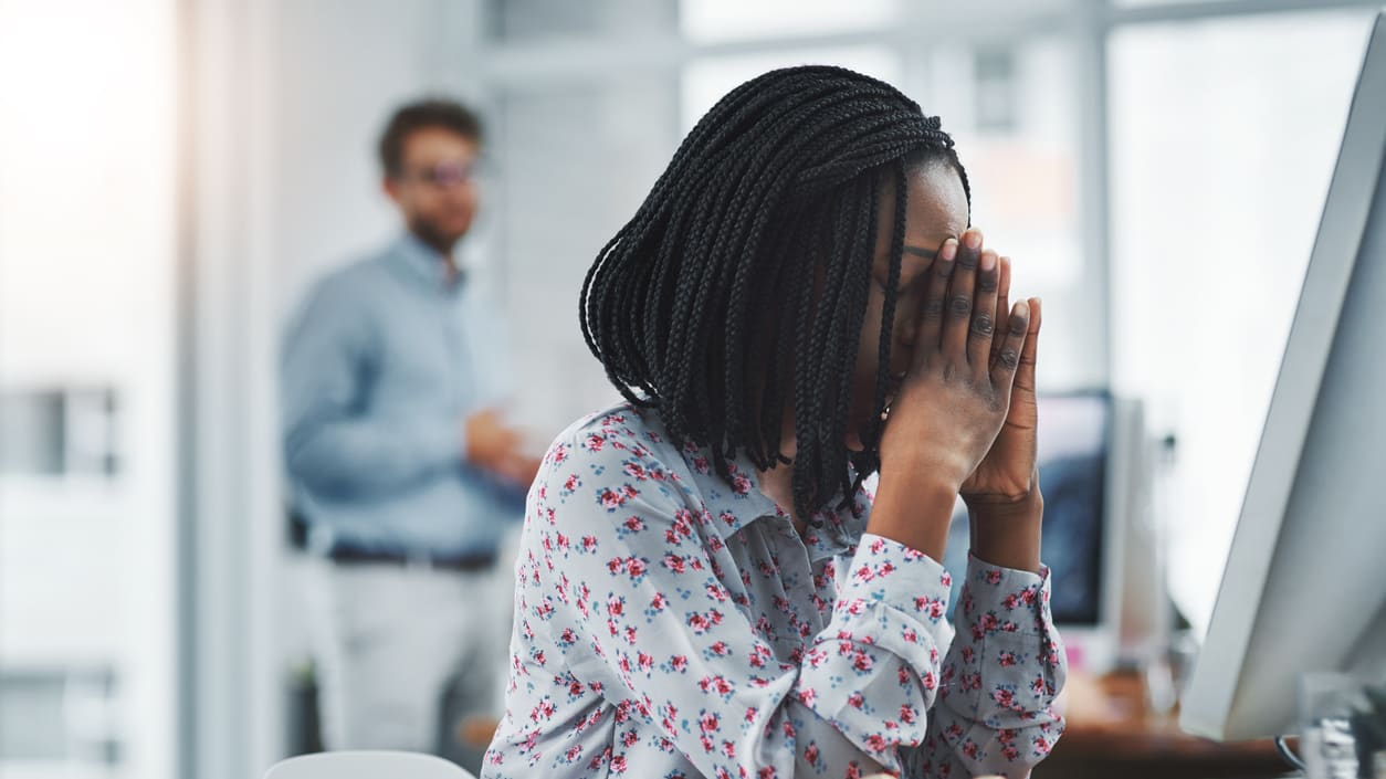 A woman covering her face in front of a computer.