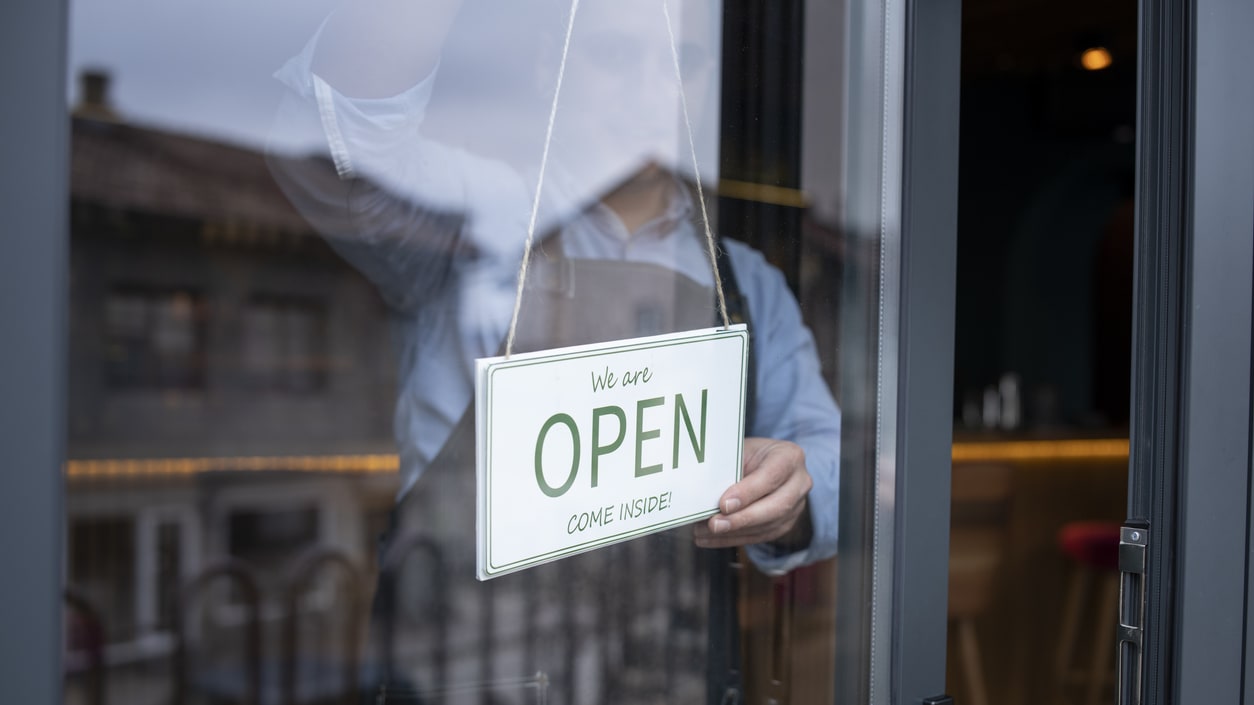 A man holding an open sign in front of a restaurant.