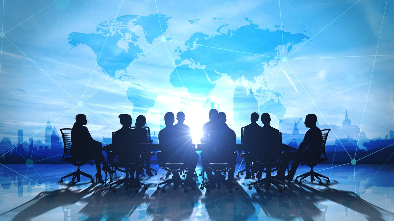 Silhouettes of business people sitting around a table in front of a world map.