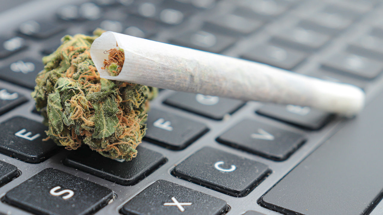 A marijuana leaf sitting on top of a laptop keyboard.