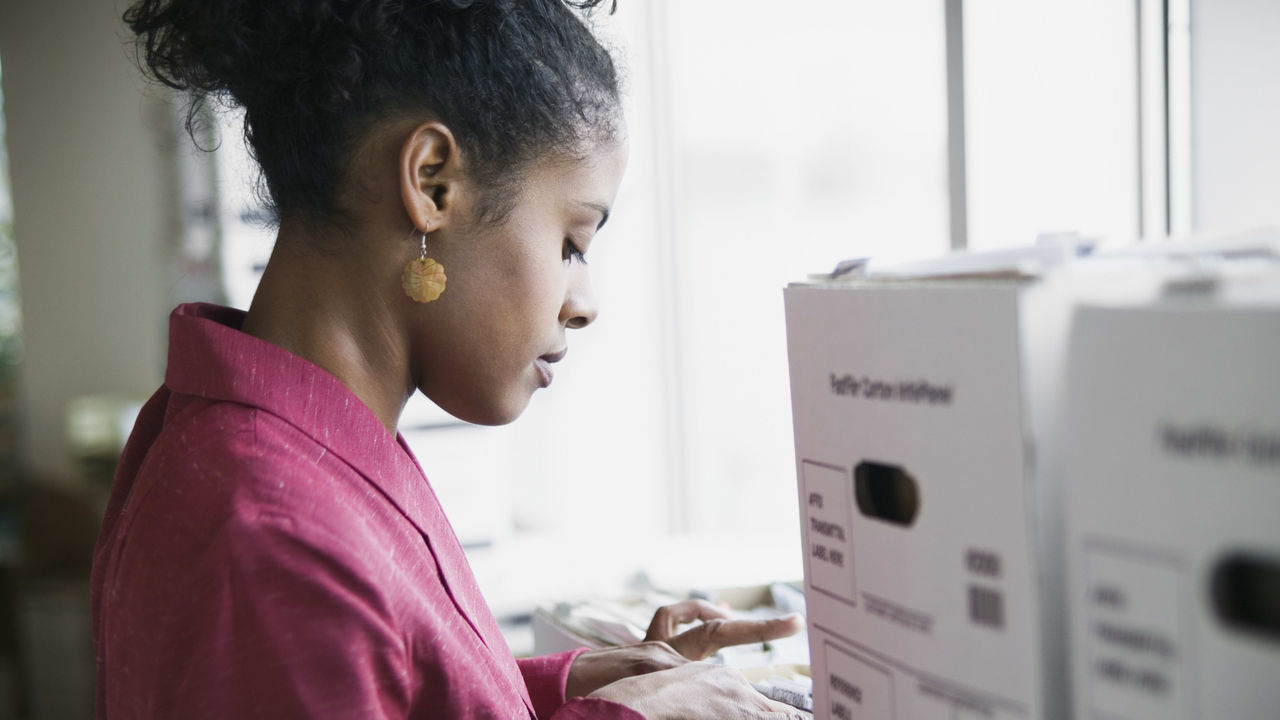 A woman is looking at a file box in an office.