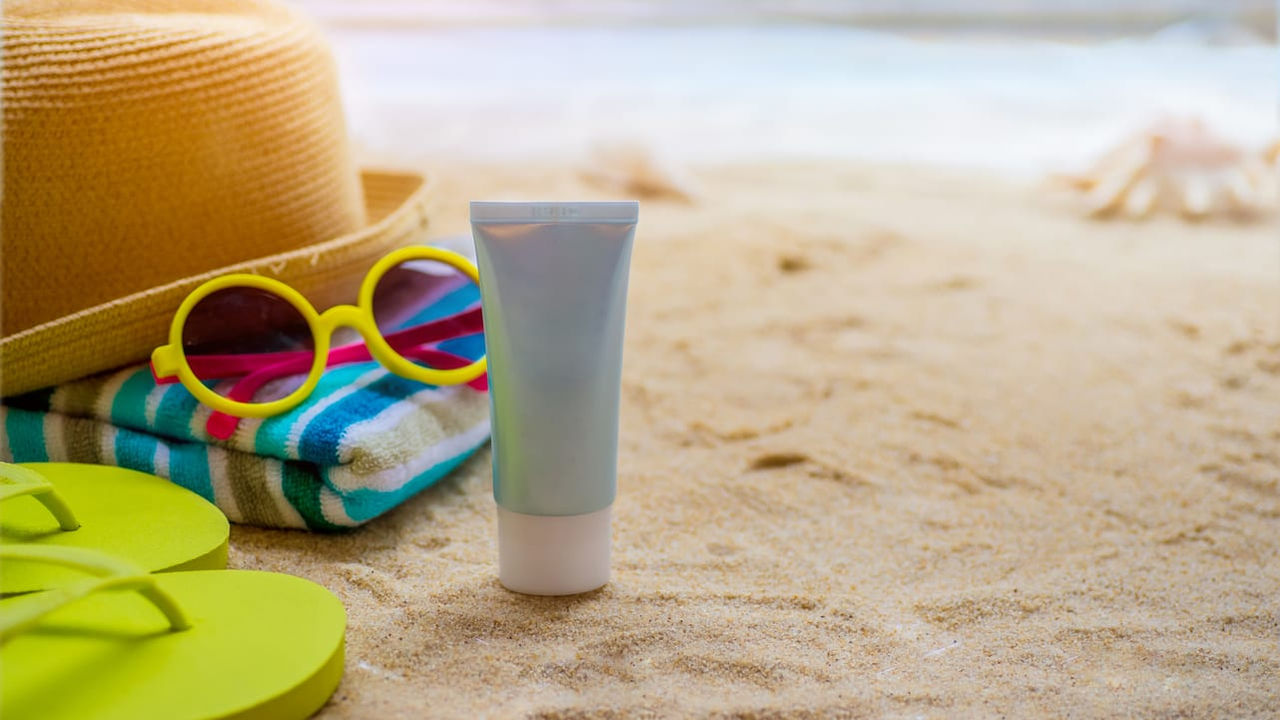 Hat, sunglasses and sunscreen on the sand.