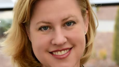 A woman in a business suit smiling in front of a window.