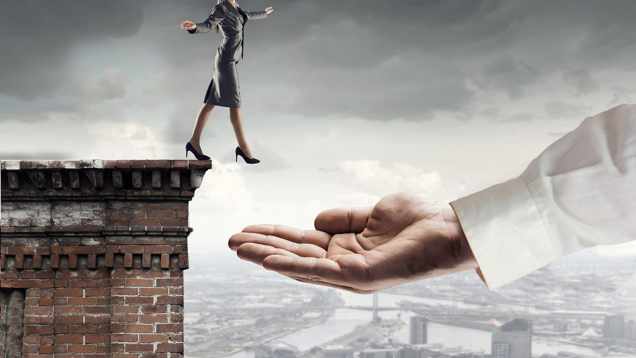 A woman is standing on top of a ledge with a hand reaching out to her.