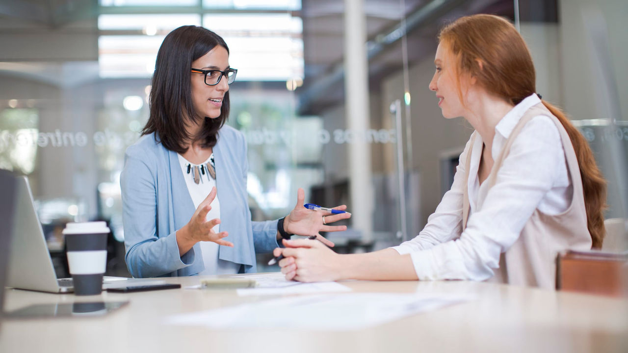 Two women talking at a table in an office.