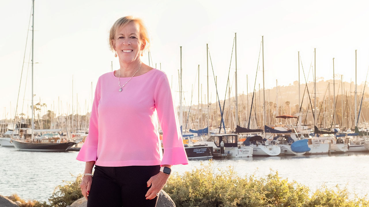 A woman in a pink shirt standing in front of a marina.