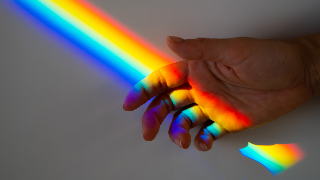 A person's hand with a rainbow light shining on it.