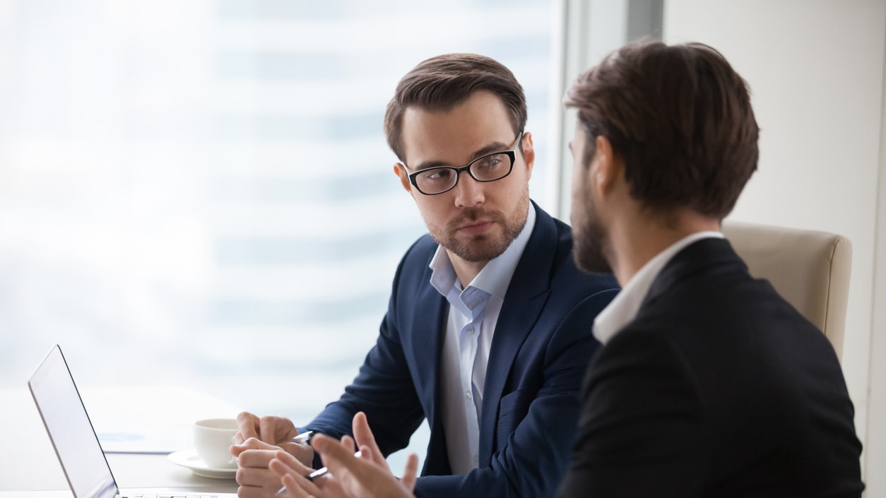 Two businessmen talking at a table in an office.