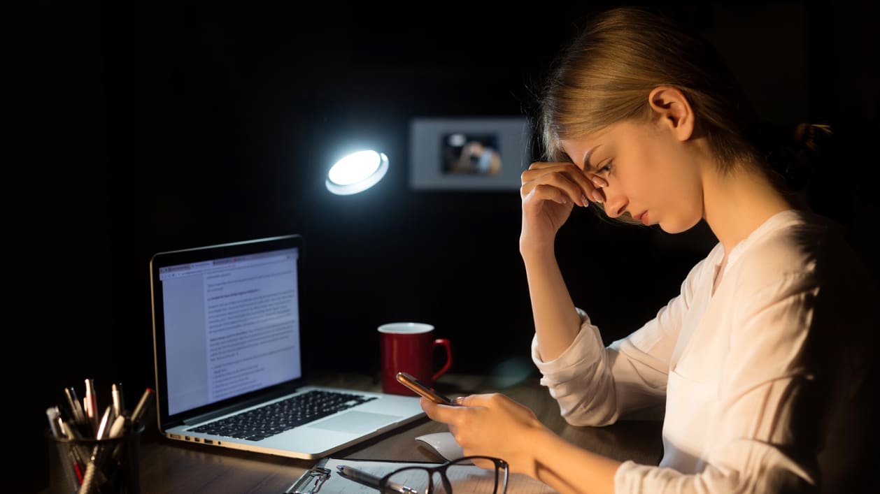 A woman is sitting at a desk with a laptop and cell phone.