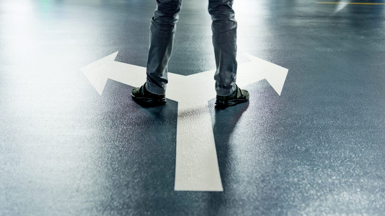 A man standing on a parking lot with two arrows pointing in different directions.