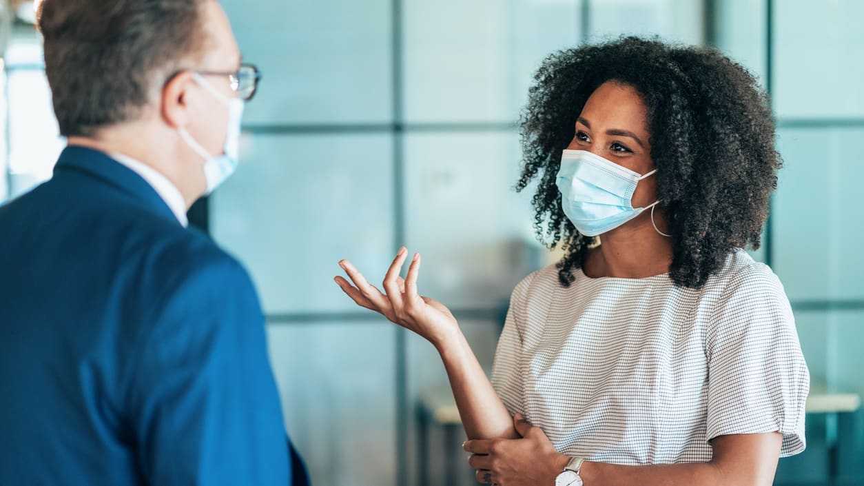 A woman wearing a surgical mask is talking to a man in an office.