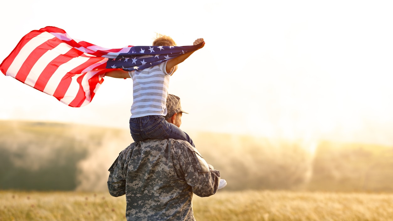 A man is holding an american flag over his head as he walks through a field.
