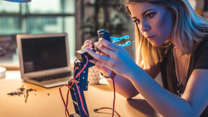 A young woman is working on a robotic arm.