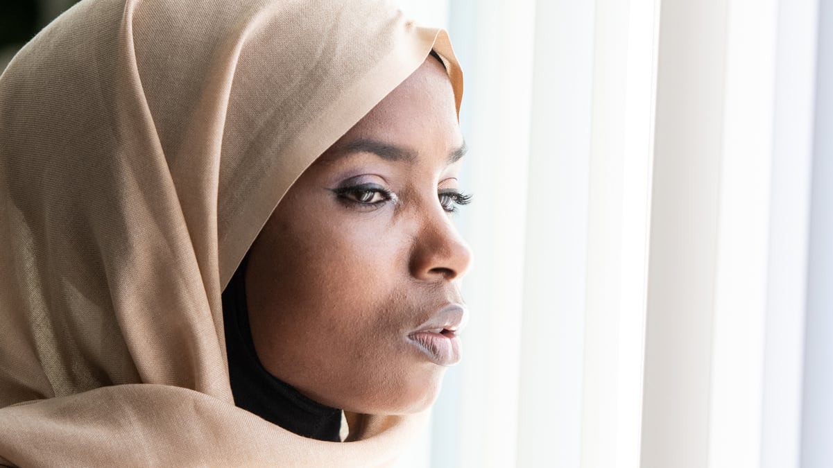 A woman in a hijab looking out a window.
