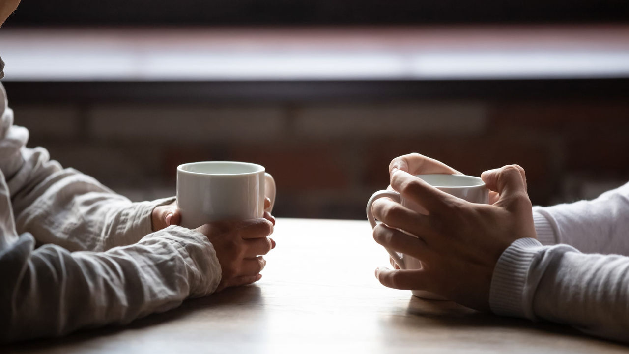 Two people holding coffee mugs at a table.