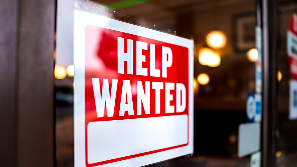 A sign that says help wanted on the door of a restaurant.