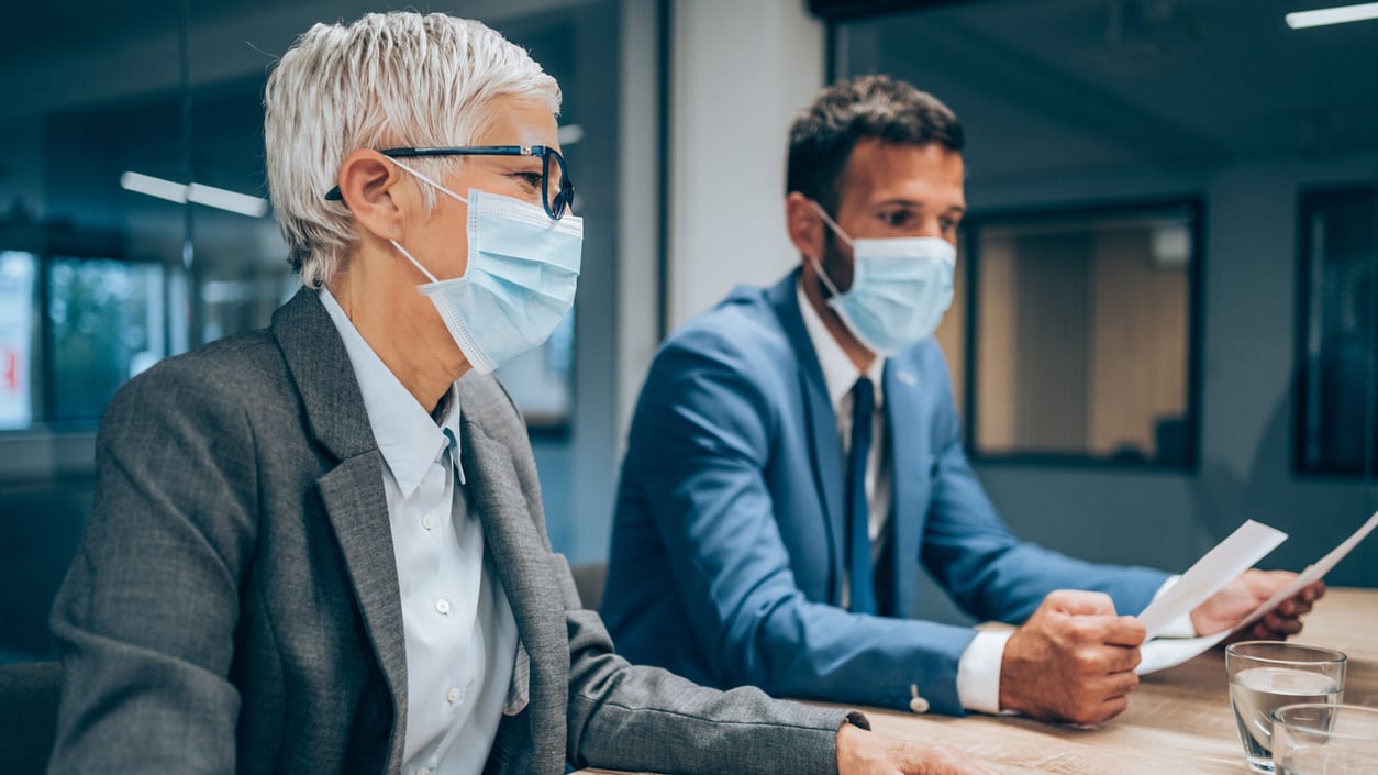 Two business people wearing surgical masks at a meeting.