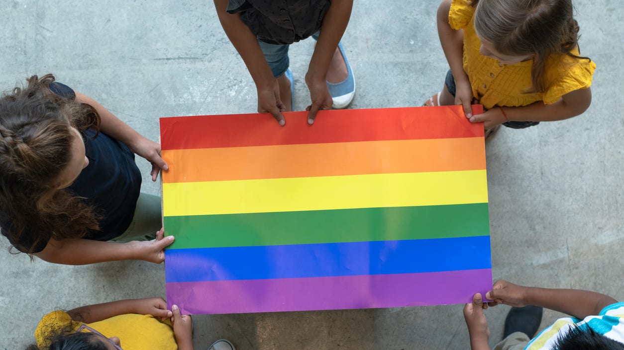 A group of children holding a rainbow flag.