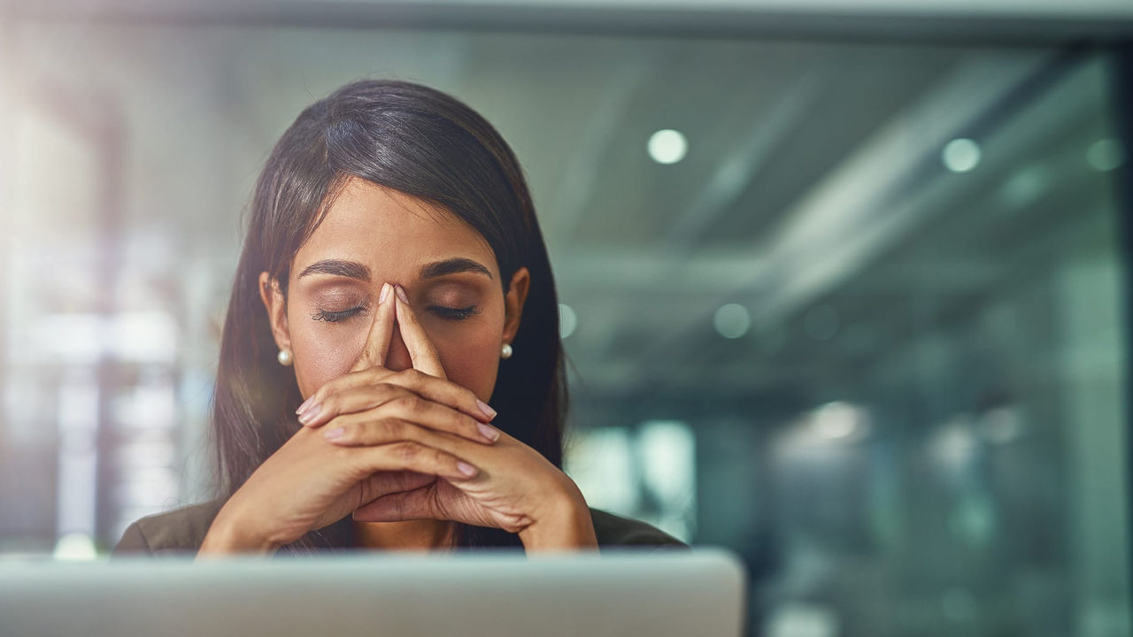 A business woman covering her nose with her hand in front of a laptop.